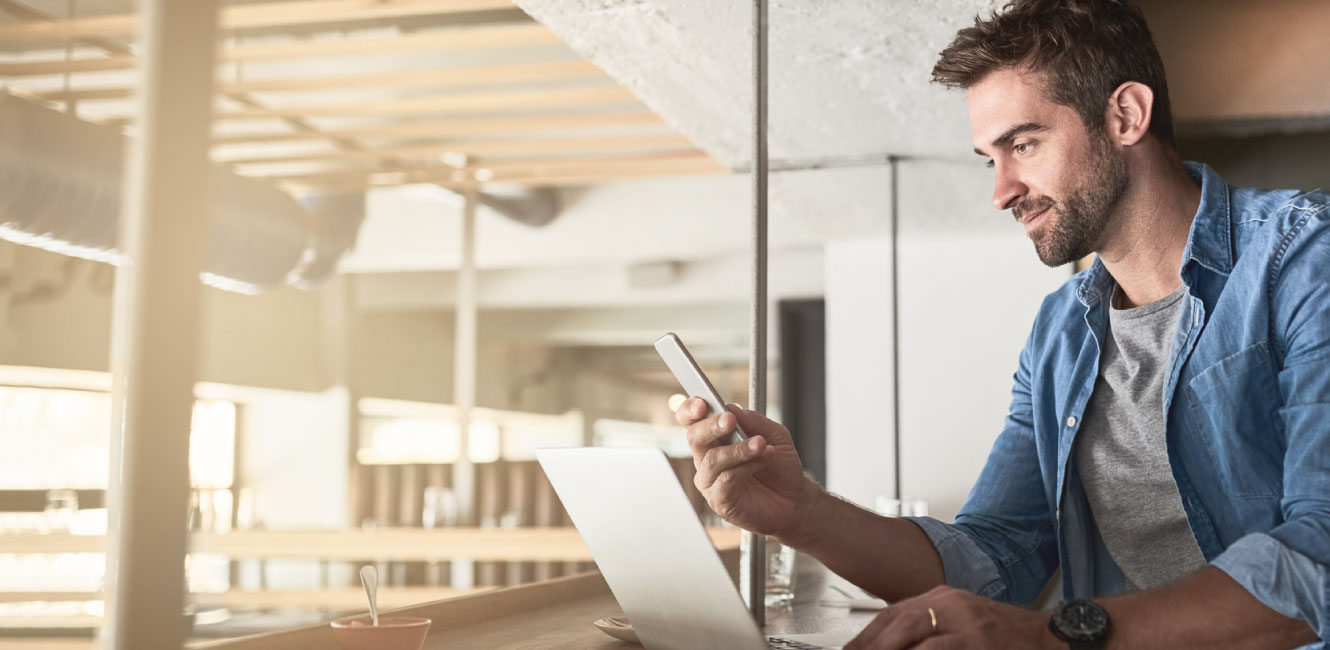 man sitting a table using his computer and smartphone 