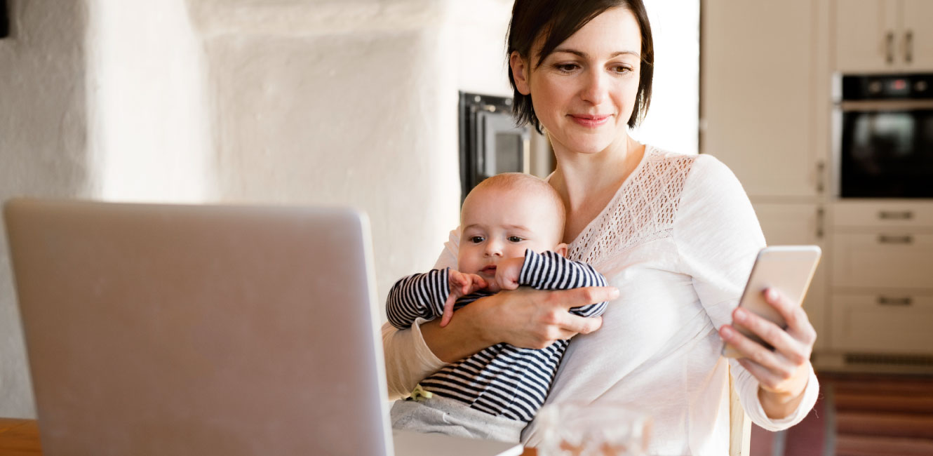 a mom holding her baby and checking her phone 